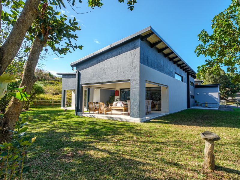 A modern rear elevation featuring a covered patio with large sliding glass doors, overlooking a well-maintained garden and lawn area.
