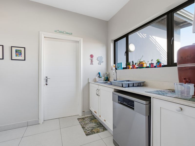 A functional laundry area featuring white built-in cabinetry, a stainless steel sink, and tiled flooring with natural light from a large window.