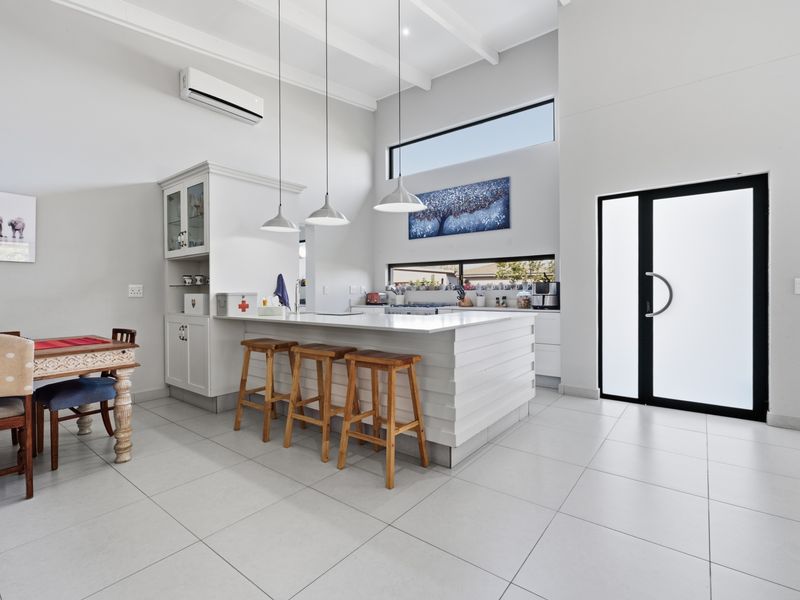 Modern open-plan kitchen featuring a central island with stone countertops, pendant lighting, high ceilings, and sleek tiled flooring, creating a bright and airy space.