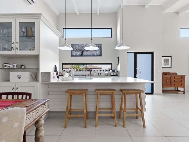 Bright open-plan kitchen featuring a central island, modern cabinetry, high ceilings with clerestory windows, and sleek tiled flooring throughout.