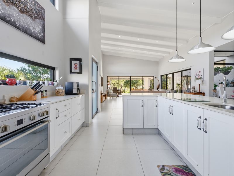 Spacious open-plan kitchen featuring white cabinetry, a central island, gas cooktop, and high vaulted ceilings, flowing seamlessly into the living area.