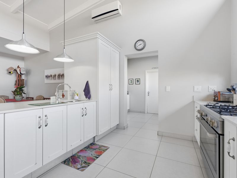 Modern kitchen featuring white cabinetry, stone countertops, gas stove, and tiled flooring, with an open-plan layout connecting to the dining area.