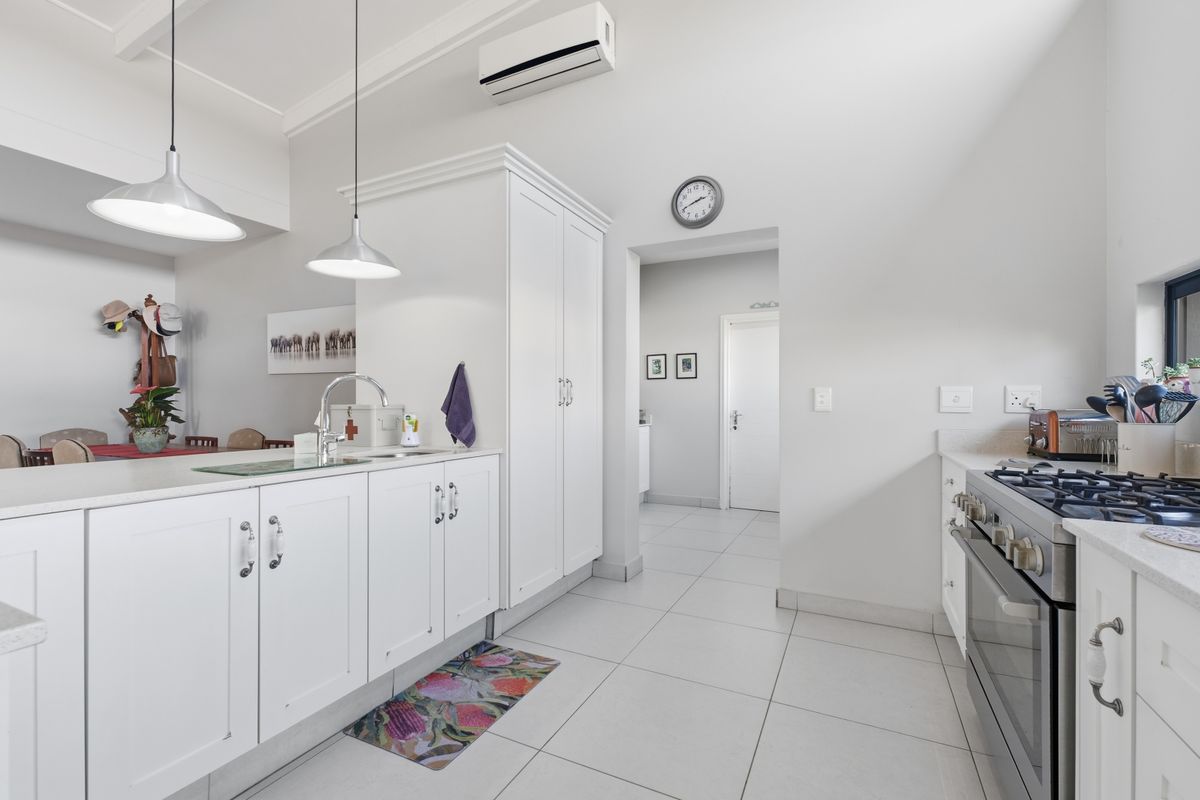 Modern kitchen featuring white cabinetry, stone countertops, gas stove, and tiled flooring, with an open-plan layout connecting to the dining area.