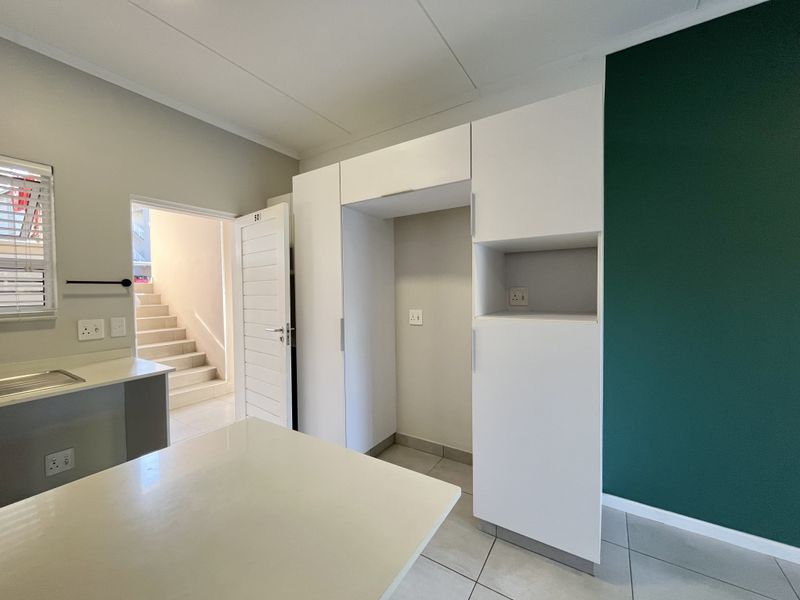 A clean, modern kitchen area featuring white built-in cabinetry, a countertop with a sink, and a striking green accent wall.