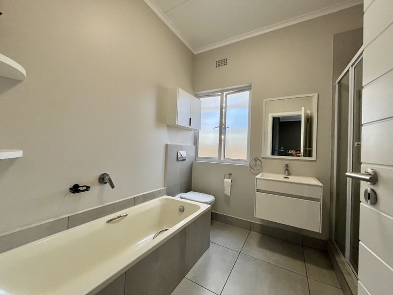 A clean, modern bathroom featuring a bathtub, separate shower enclosure, wall-mounted vanity, and wall-hung toilet with neutral tiling.