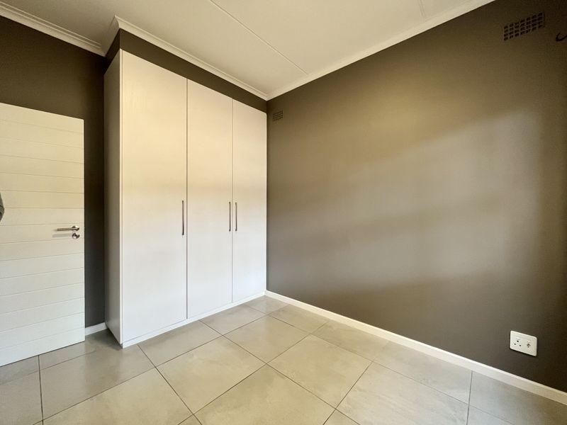 A clean, empty bedroom featuring neutral grey walls, large format floor tiles, and a modern white built-in wardrobe.