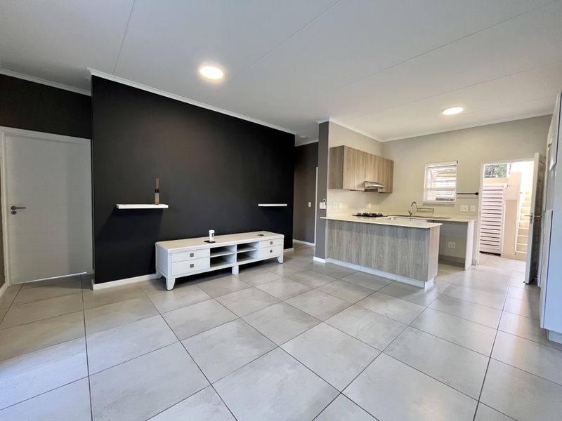 Modern open-plan living area featuring large format floor tiles, a contemporary kitchen with wood-finish cabinetry, and a striking dark feature wall.