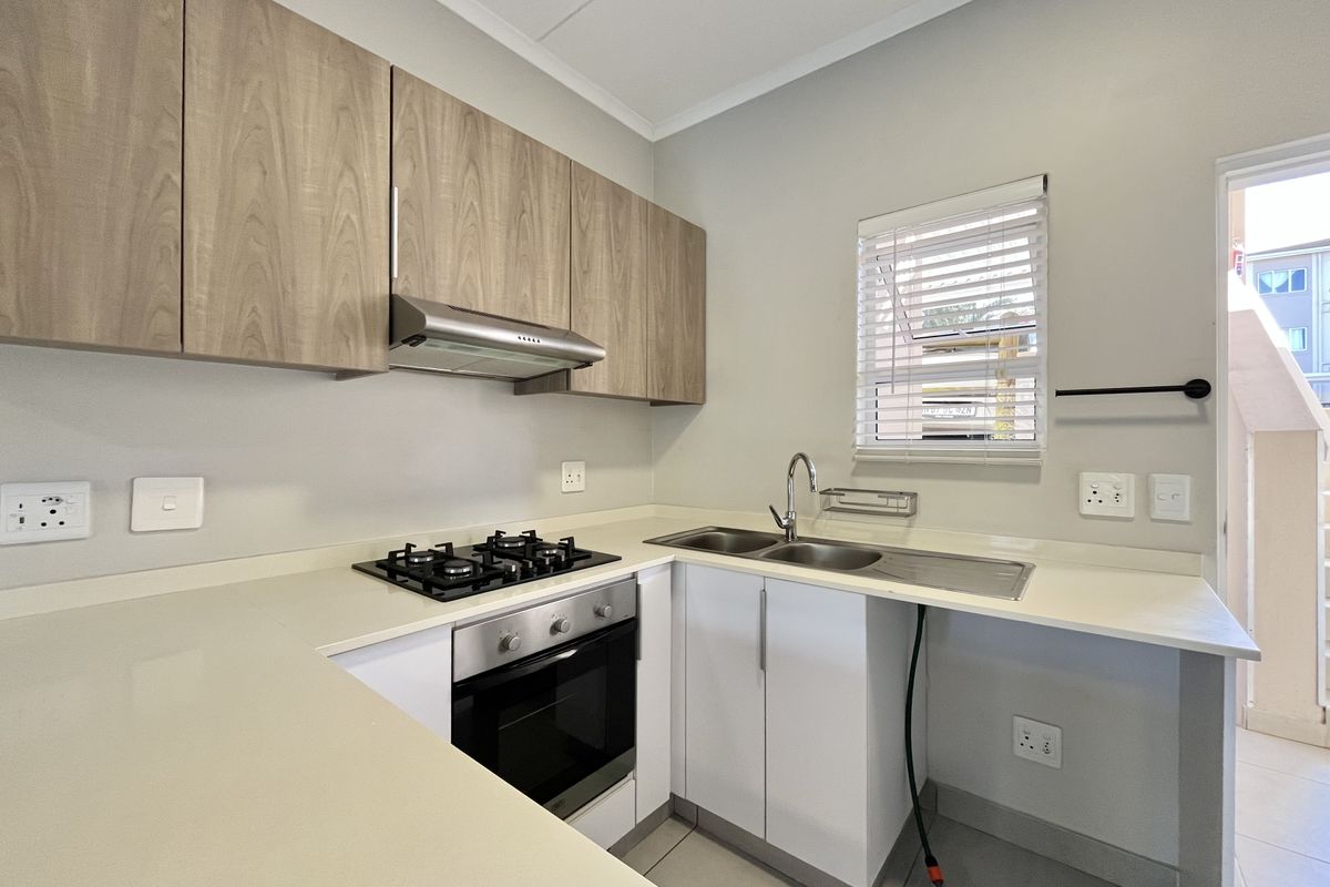 Modern kitchen featuring light wood-grain cabinetry, stone countertops, a gas hob, built-in oven, and a double sink with a window view.