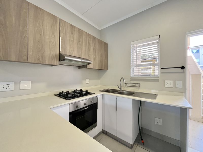 Modern kitchen featuring light wood-grain cabinetry, stone countertops, a gas hob, built-in oven, and a double sink with a window view.