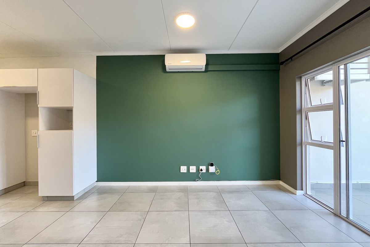 A bright, open-plan living area featuring large-format floor tiles, a feature wall with a mounted air conditioner, and direct access to an outdoor space.