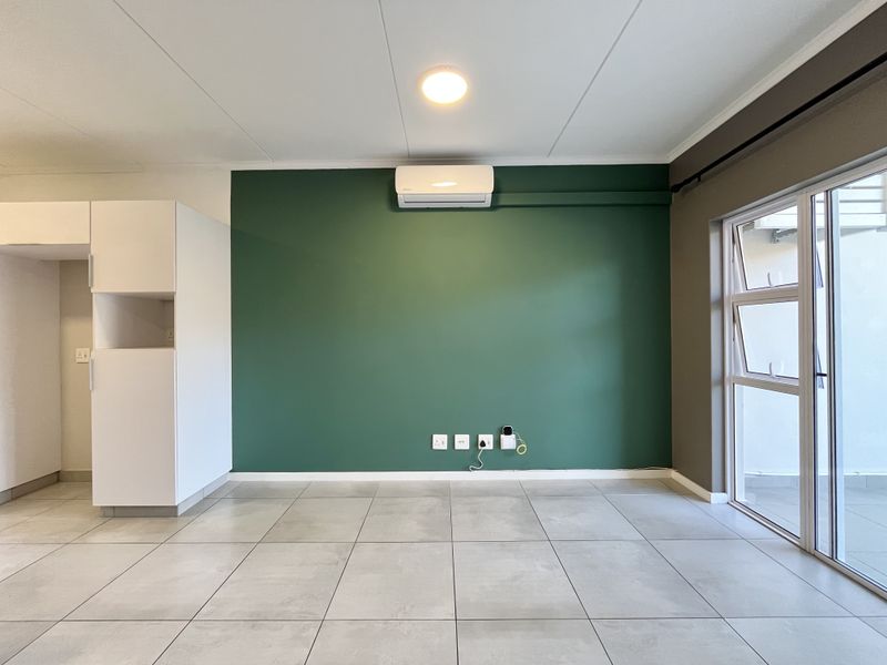 A bright, open-plan living area featuring large-format floor tiles, a feature wall with a mounted air conditioner, and direct access to an outdoor space.