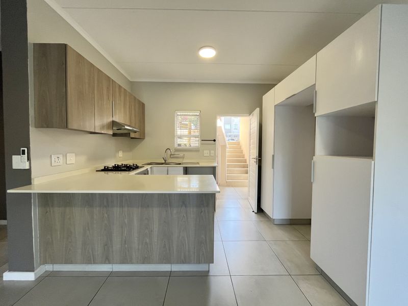 Modern kitchen featuring wood-grain and white cabinetry, stone countertops, gas hob, extractor fan, and tiled flooring, leading to an external staircase.