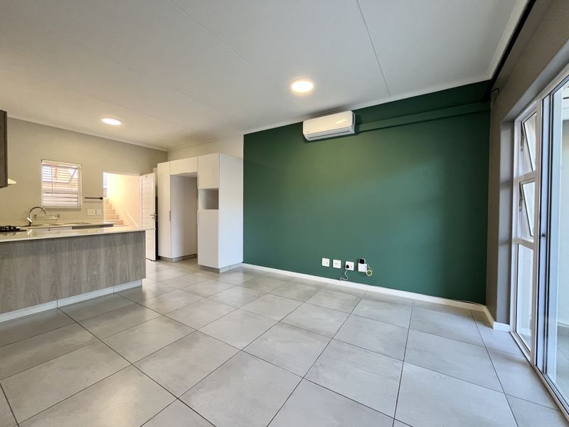 Spacious open-plan living area featuring tiled floors, a modern kitchen with island, and a split-system air conditioner, leading to a bright outdoor space.