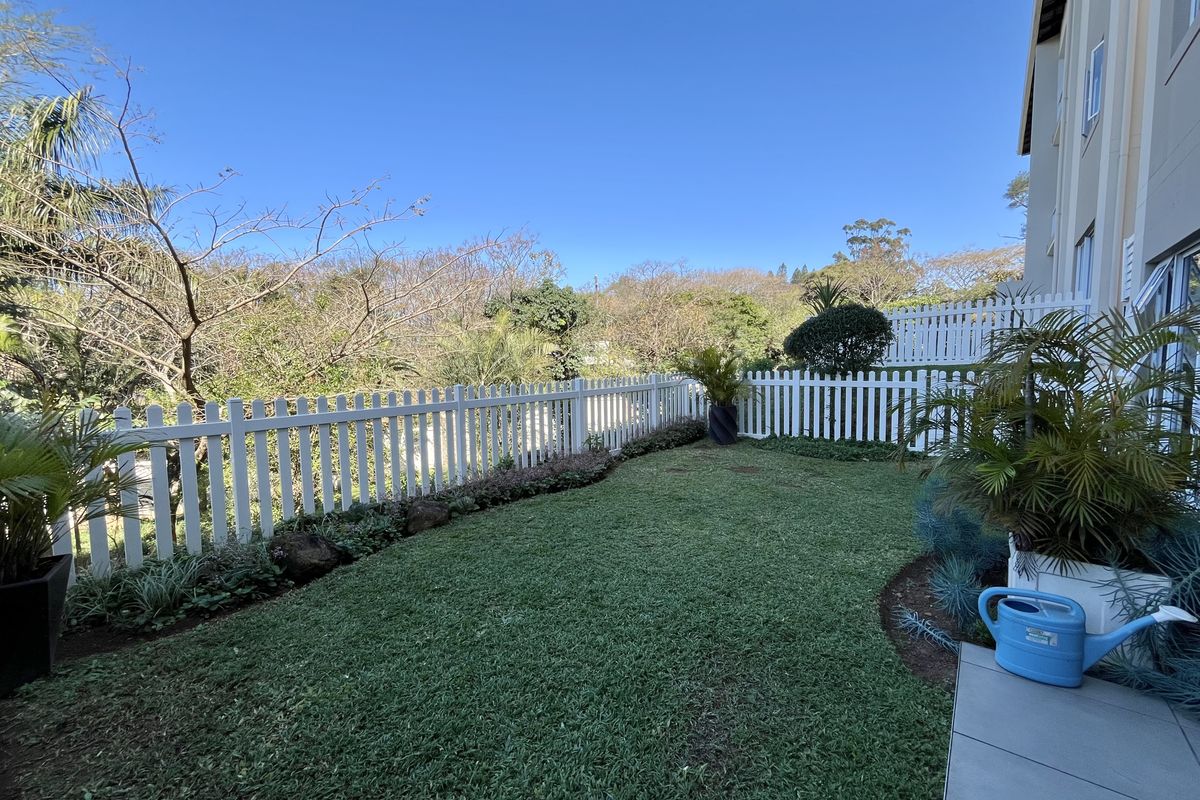 A well-maintained rear garden featuring a neat lawn, landscaped borders, and a white picket fence, complemented by a paved patio area.
