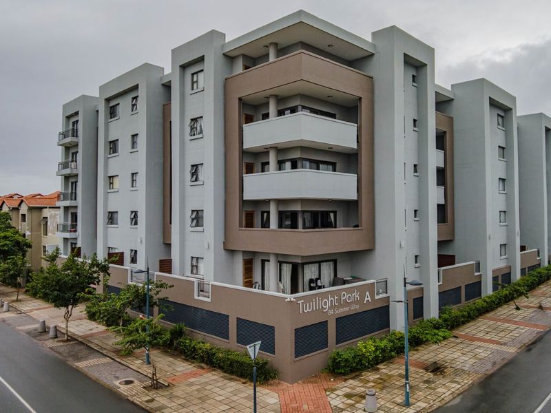 A modern multi-story apartment complex exterior featuring balconies and a perimeter wall, situated on a corner lot with street access.