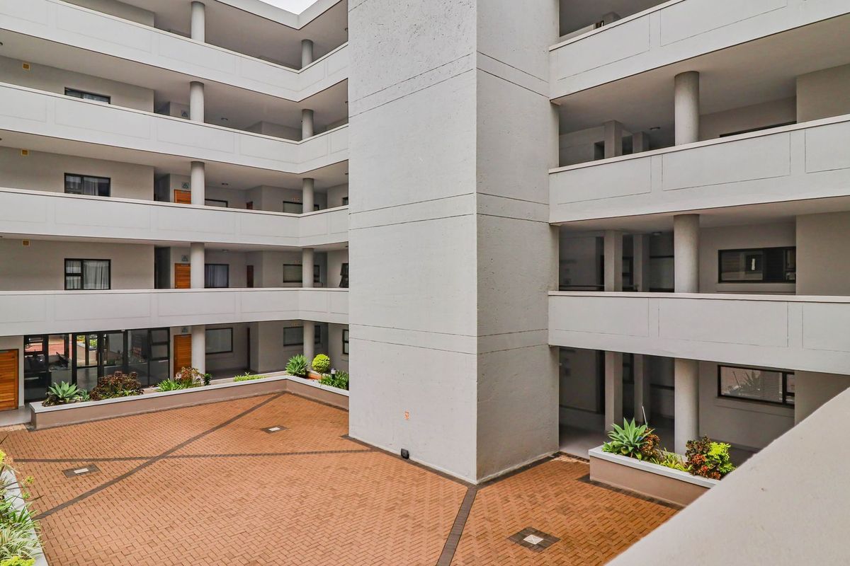 A view of the apartment complex central courtyard featuring paved flooring, concrete structural columns, and integrated planter boxes.