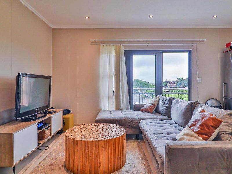 A well-lit living room featuring tiled flooring, recessed downlights, and a sliding glass door providing access to the balcony.