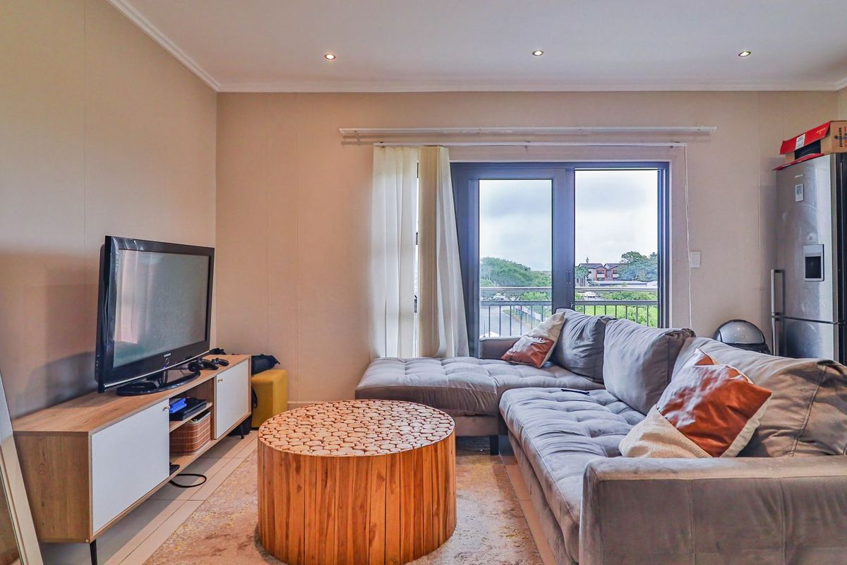 A well-lit living room featuring tiled flooring, recessed downlights, and a sliding glass door providing access to the balcony.