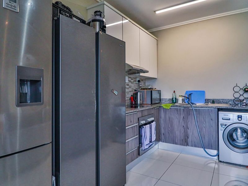 Compact kitchen featuring modern cabinetry, granite countertops, tiled backsplash, and integrated laundry plumbing, providing a functional and efficient workspace.