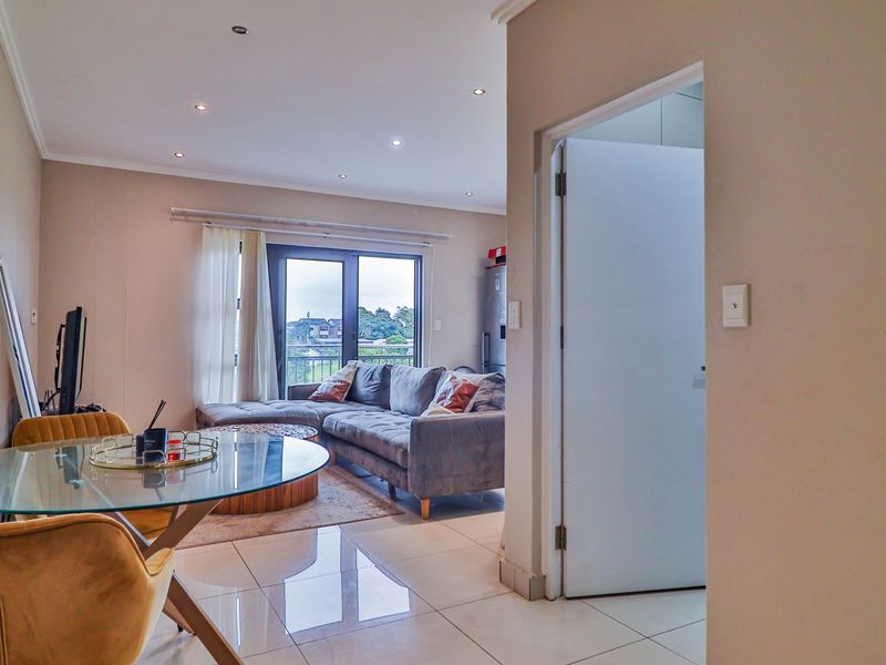 An open-plan living and dining area featuring polished tile flooring, recessed lighting, and a sliding glass door leading to a balcony.