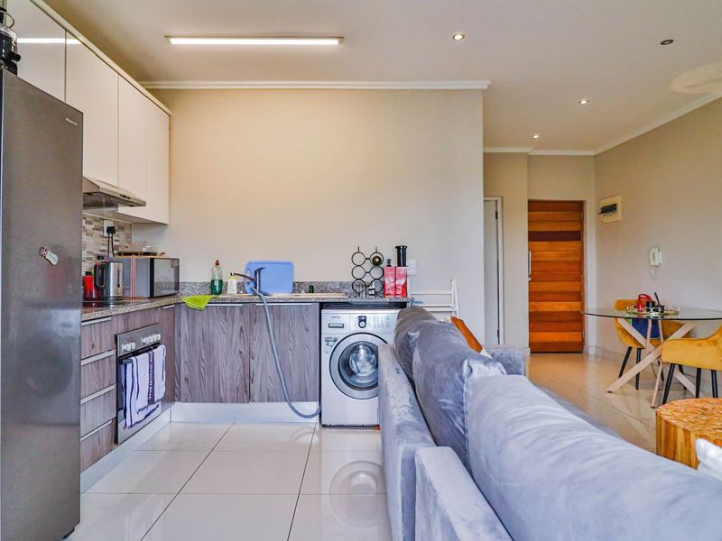 Open-plan living area featuring a modern kitchen with granite countertops, built-in cabinetry, and integrated laundry plumbing, flowing into a bright dining and lounge space.