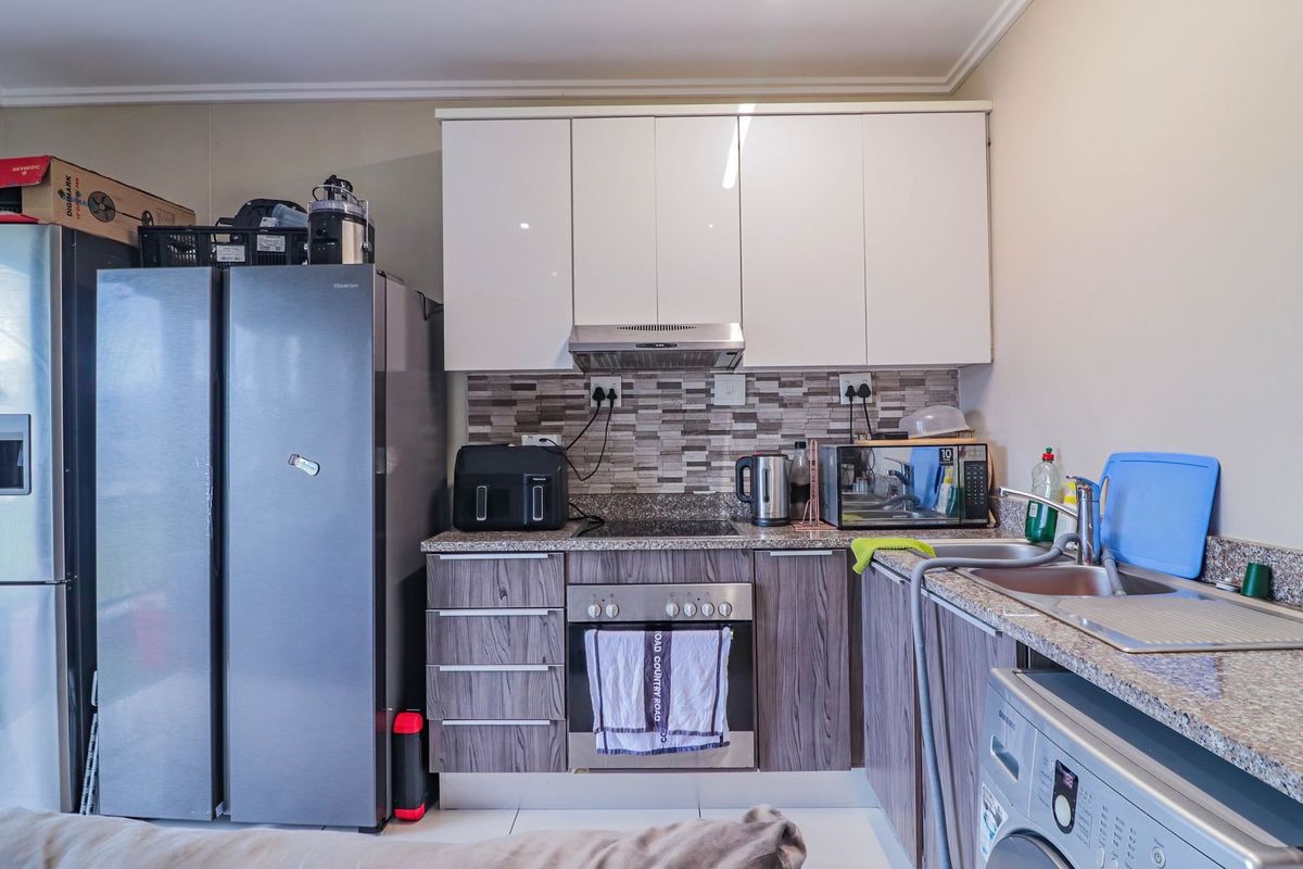 A functional kitchen featuring modern wood-grain lower cabinets, white upper cabinetry, granite countertops, and a mosaic tile backsplash with integrated appliances.