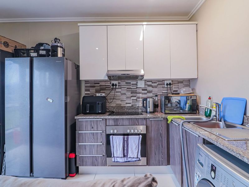 A functional kitchen featuring modern wood-grain lower cabinets, white upper cabinetry, granite countertops, and a mosaic tile backsplash with integrated appliances.