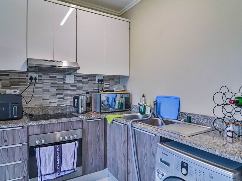 A compact, functional kitchen featuring granite countertops, built-in cabinetry, a stainless steel oven, hob, and extractor fan with a modern tiled backsplash.