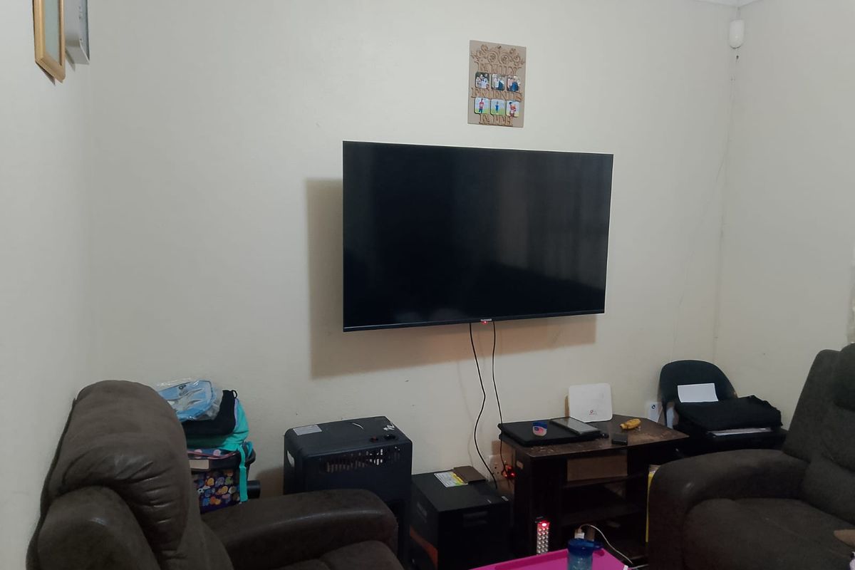 A living room area featuring a wall-mounted television and neutral wall finishes, providing a functional space for entertainment.