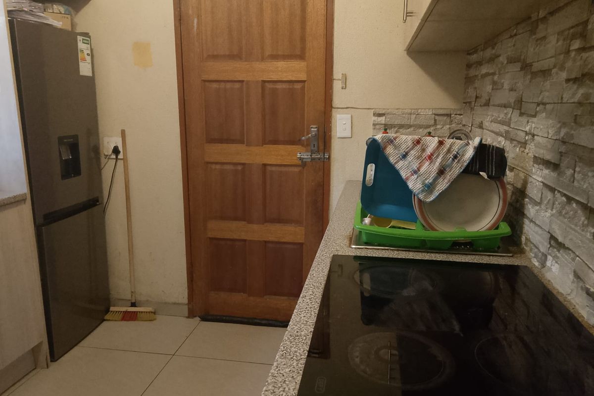 A functional kitchen area featuring a built-in electric hob, stone-look splashback, and tiled flooring, requiring minor cosmetic updates to the wall finishes.