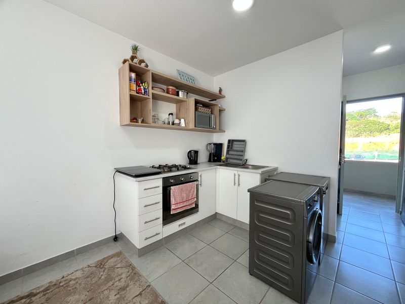 Compact kitchen featuring built-in cabinetry, gas hob, oven, stainless steel sink, and tiled flooring with adjacent laundry space.