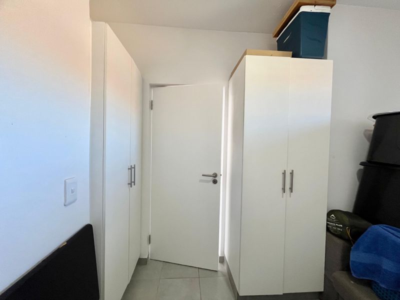 A functional hallway featuring white built-in cupboards and neutral tiled flooring, providing efficient storage space within the apartment.