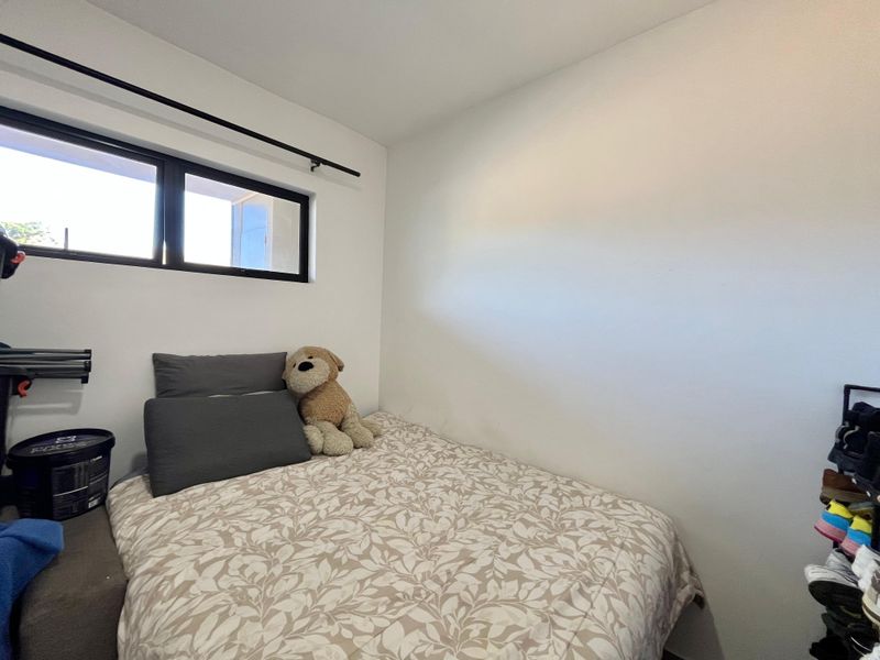 A compact bedroom featuring a black-framed window and neutral wall finishes, providing a functional space for a single bed.