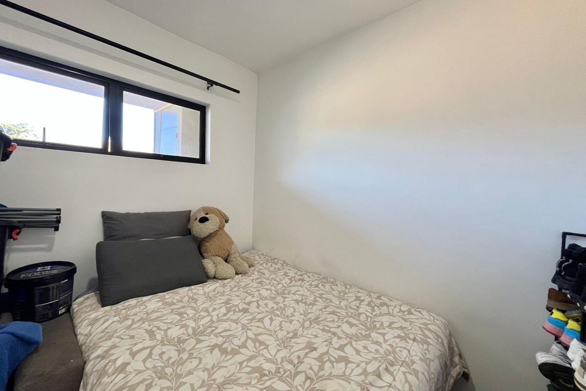 A compact bedroom featuring a black-framed window and neutral wall finishes, providing a functional space for a single bed.