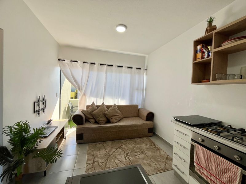 Compact open-plan living area featuring a functional kitchen with built-in oven and hob, leading directly to a small balcony through a sliding glass door.