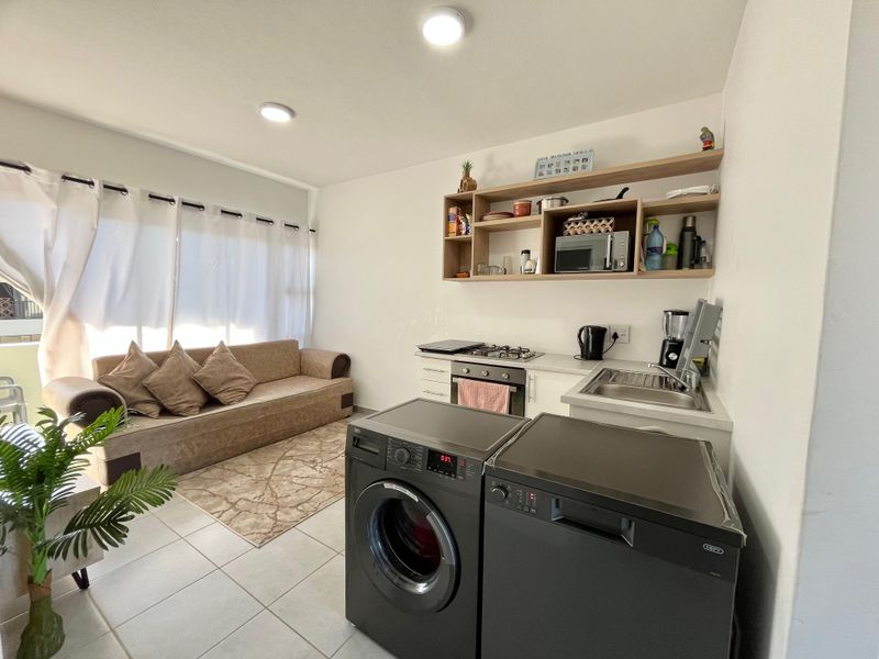An open-plan living and kitchen area featuring tiled floors, fitted cabinetry, a gas hob, built-in oven, and stainless steel sink.
