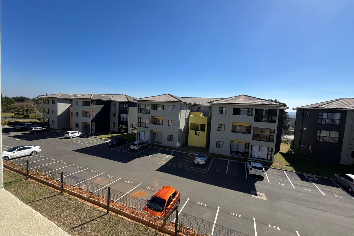 Aerial view of an apartment complex featuring multiple multi-story residential buildings, paved parking areas, and perimeter fencing under a clear sky.
