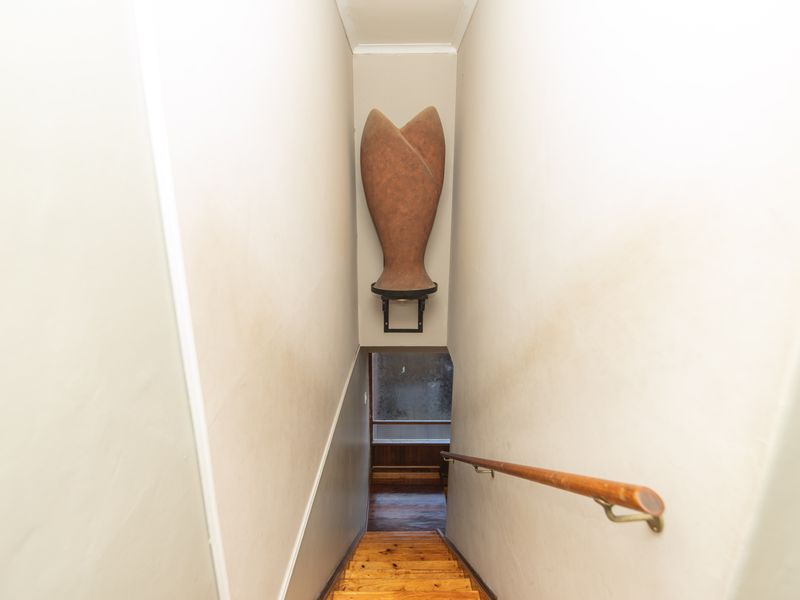A narrow staircase hallway featuring wooden steps and a timber handrail, showing signs of wear on the wall surfaces.