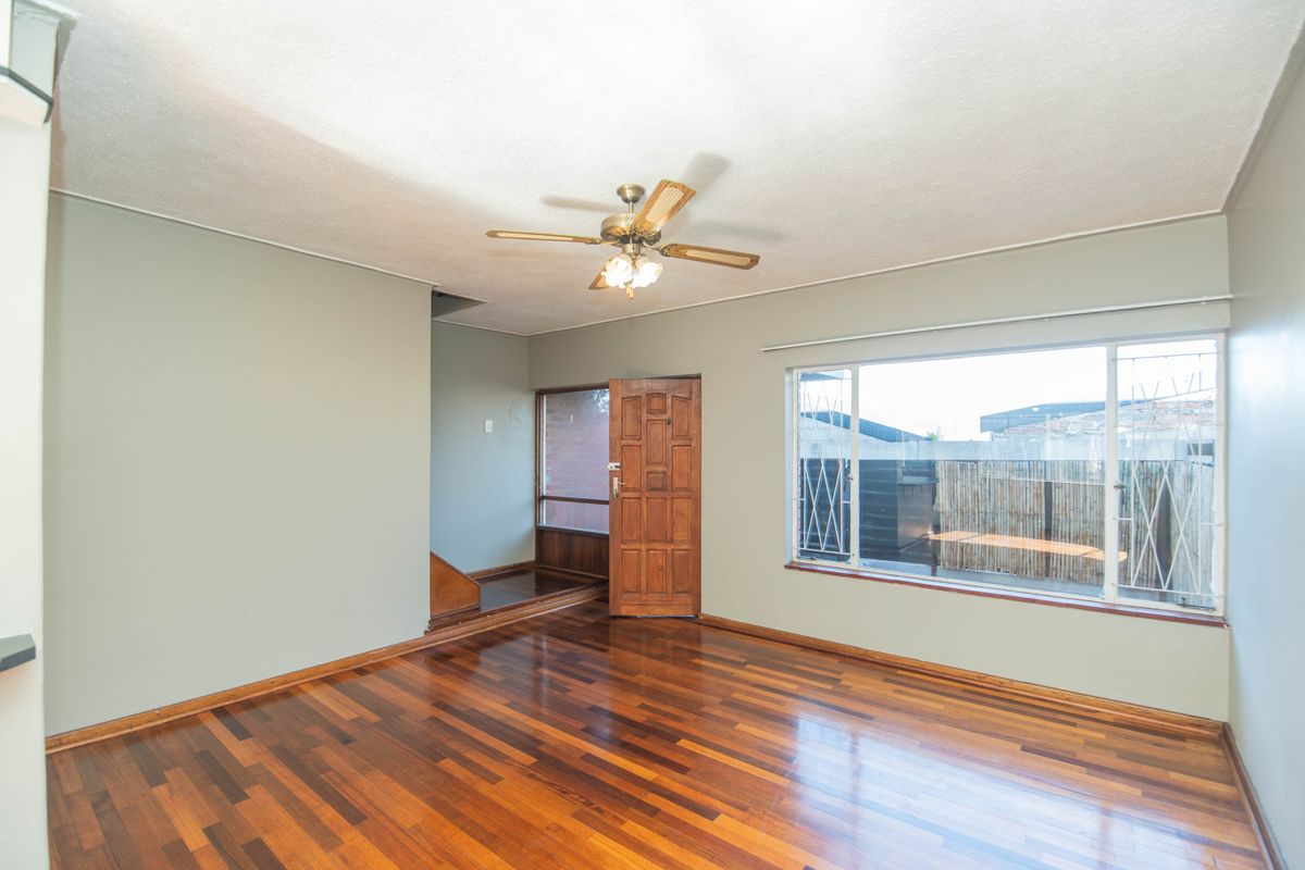 Spacious living area featuring polished hardwood flooring, a ceiling fan, and large windows with security bars, offering a bright and open layout.