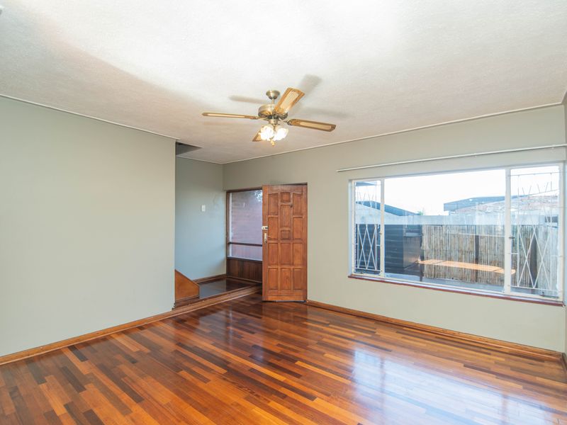 Spacious living area featuring polished hardwood flooring, a ceiling fan, and large windows with security bars, offering a bright and open layout.