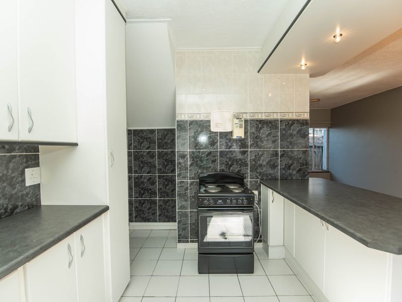 A functional kitchen featuring white cabinetry, dark laminate countertops, tiled splashbacks, and a freestanding stove, offering a clean and practical workspace.