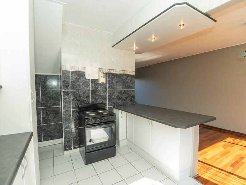 A functional kitchen area featuring tiled splashbacks, built-in cabinetry, a breakfast bar, and a freestanding stove, opening into an adjacent living space.