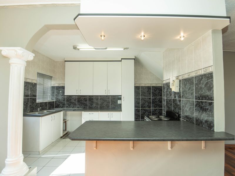 A functional kitchen featuring white cabinetry, dark tiled backsplashes, a breakfast bar, and tiled flooring, offering a clean space ready for modern updates.