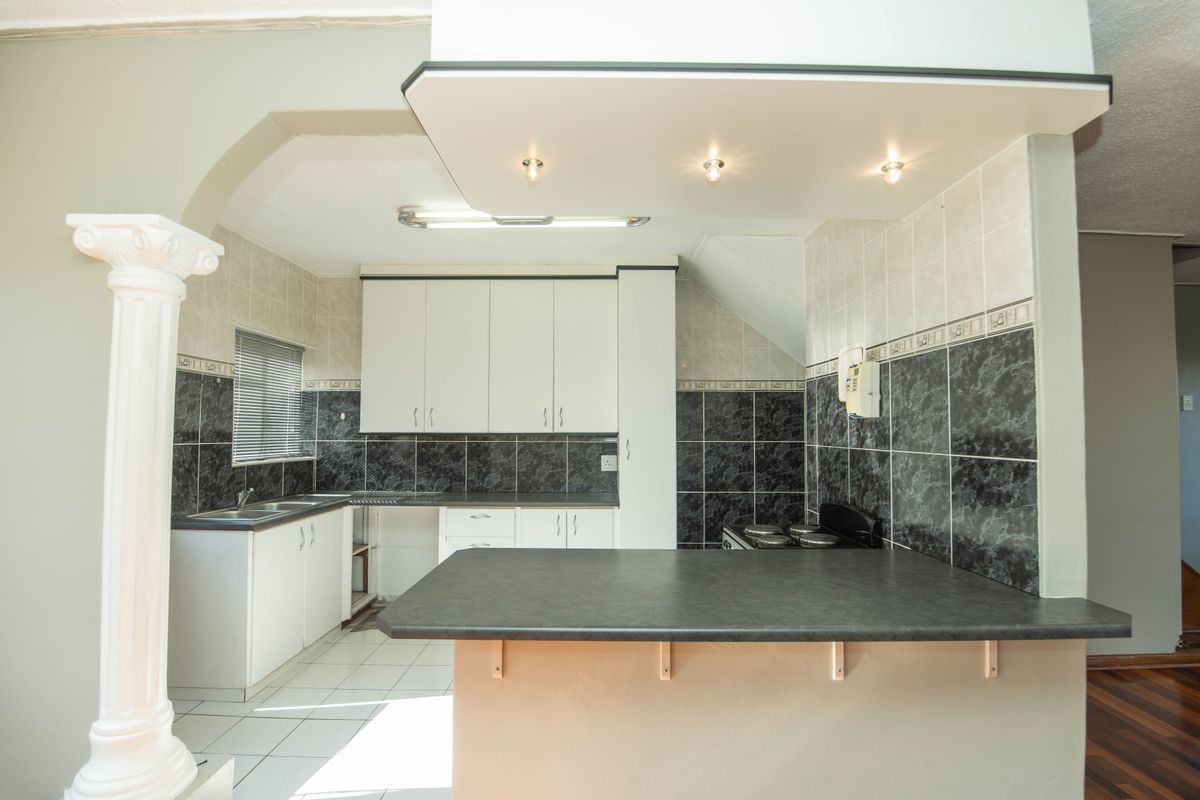 A functional kitchen featuring white cabinetry, dark tiled backsplashes, a breakfast bar, and tiled flooring, offering a clean space ready for modern updates.