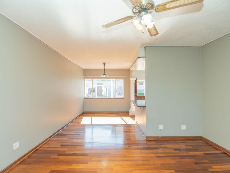 Spacious open-plan living area featuring polished hardwood flooring, a ceiling fan, and a breakfast bar connecting to the kitchen space.