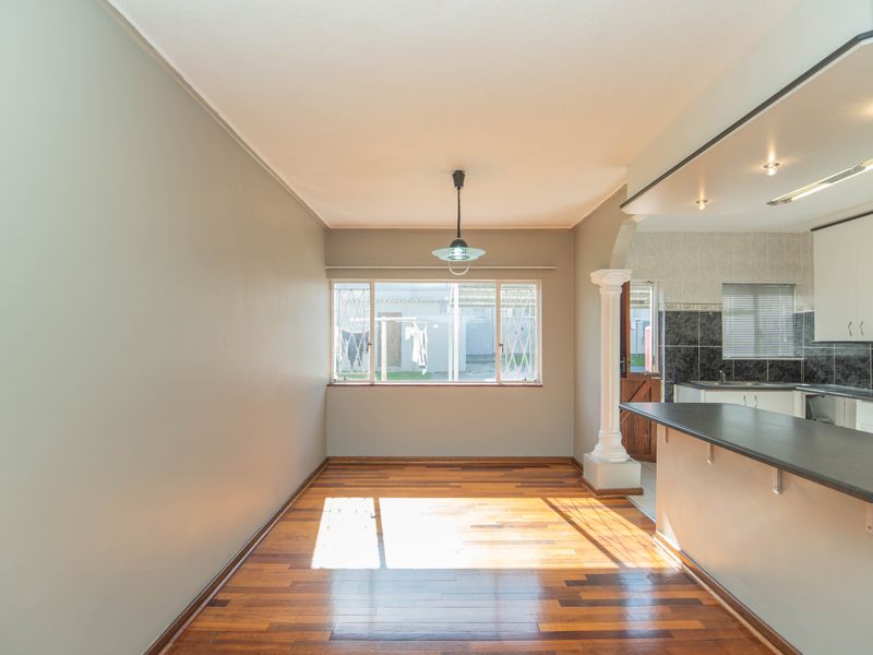 An open-plan living and dining area featuring polished hardwood floors, a breakfast bar, and a decorative column, seamlessly connecting to the kitchen space.