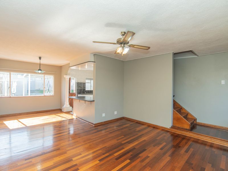 Spacious open-plan living area featuring polished hardwood flooring, a breakfast bar, and a staircase leading to the upper level.