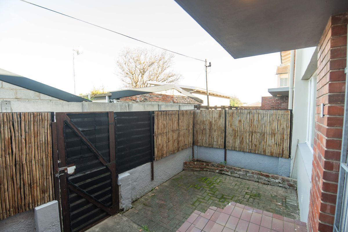 A private rear courtyard featuring brick paving, a pedestrian gate, and bamboo privacy fencing, offering a compact outdoor space for the townhouse.