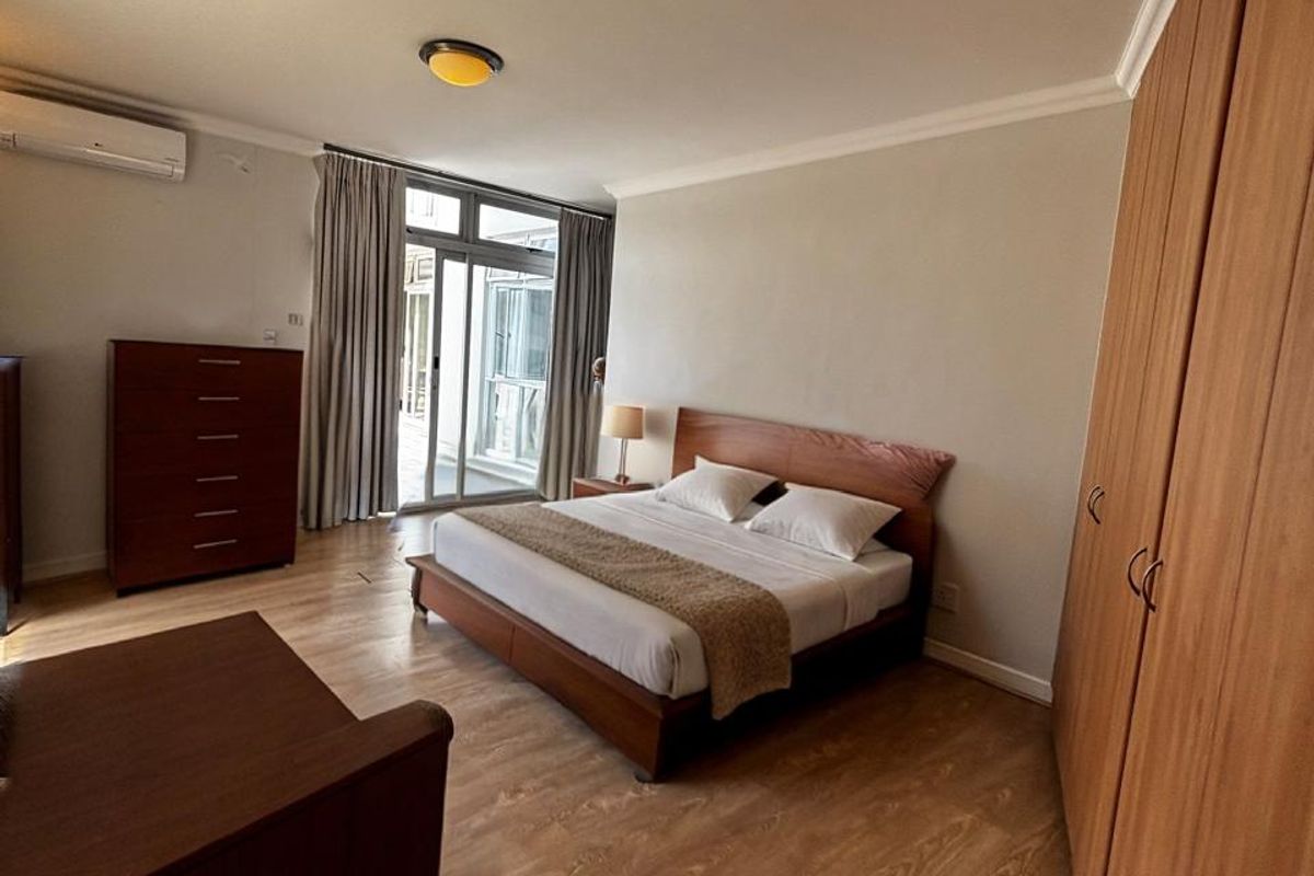 A well-maintained bedroom featuring laminate flooring, built-in wooden cupboards, a split-system air conditioner, and access to a private balcony through sliding glass doors.