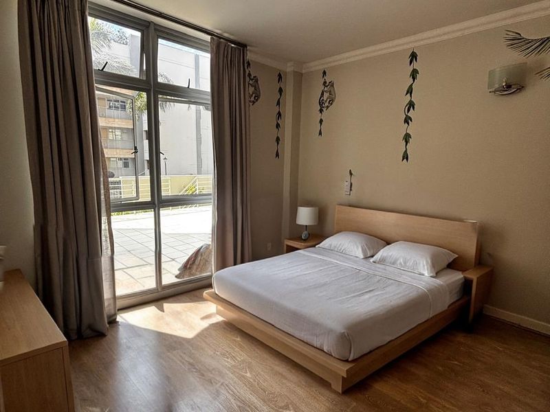 A well-lit bedroom featuring laminate flooring, a large sliding glass door providing natural light, and neutral wall finishes.